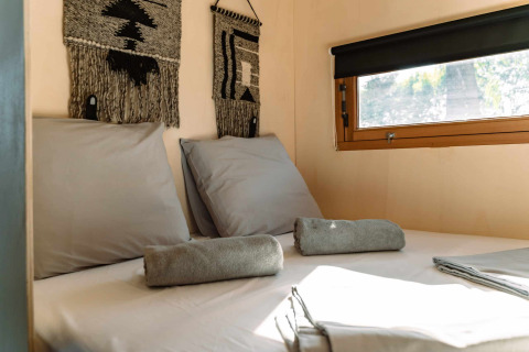 Knus bed met grijs beddengoed en handdoeken in een glamping tent bij Camping Parco Ibiza, San Antonio, Ibiza.