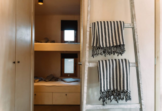 Interieur van Camping Parco Ibiza glamping met stapelbedden, ladder en gestreepte handdoeken.
