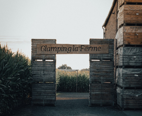 Entrée de Glamping la Ferme avec une pancarte en bois rustique entourée de champs de maïs en Flandre.