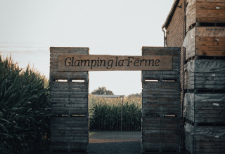 Eingang zu Glamping la Ferme mit Holzschildern und Feldern im Hintergrund in Westflandern.