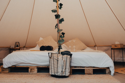 Indbydende glampingtelt med dobbeltseng, hyggelige puder og naturlige dekorationer hos Glamping La Ferme.