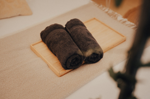 Two rolled dark towels on a wooden tray, part of the luxury camping experience at Glamping La Ferme, West Flanders.