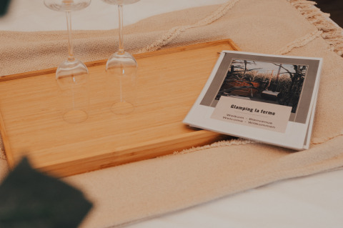 Due bicchieri da vino su un vassoio di legno accanto a una brochure di benvenuto di Glamping La Ferme in West-Vlaanderen.