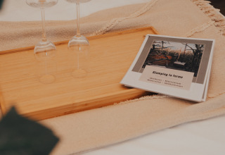 Zwei Weingläser auf einem Holztablett neben einer Glamping La Ferme-Willkommensbroschüre in Westflandern.