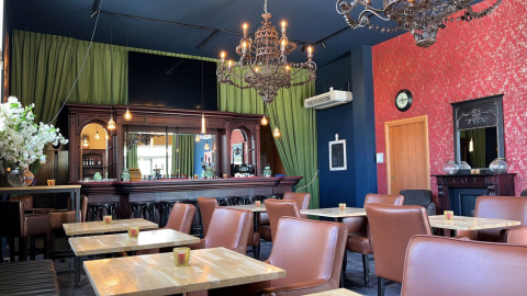 Elegant restaurantindretning med brune stole, lysekroner og grønne gardiner på Per Amore Del Vino i Lombardiet.