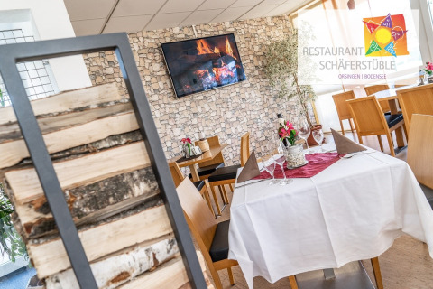 Cozy interior of Restaurant Schäferstüble with stone walls, wood stacks and tastefully set dining tables.
