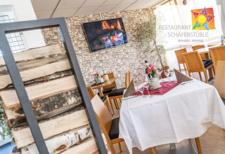 Gezellige inrichting van Restaurant Schäferstüble met stenen muur, houtstapels en sfeervol gedekte tafels.