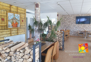 Interno di ristorante con legna accatastata, tavoli in legno, parete in pietra e dipinto pecora mascotte.