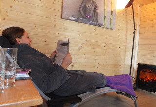 Vrouw ontspant op ligstoel en leest tijdschrift in een knusse houten hut bij Camping & Vakantiepark Orsingen.