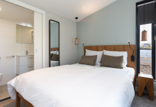 Dormitorio moderno en una lodge de lujo con cama doble, baño y vista al lago en Friesland.