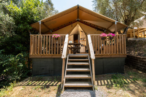 Glamping accommodatie DivaCamp San Marino met safaritent, houten veranda en bloembakken in een groene omgeving.