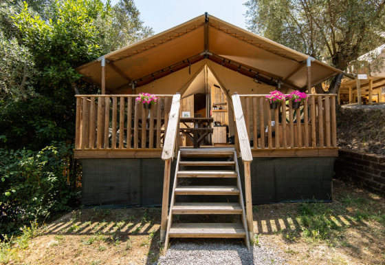 Glamping accommodatie DivaCamp San Marino met safaritent, houten veranda en bloembakken in een groene omgeving.