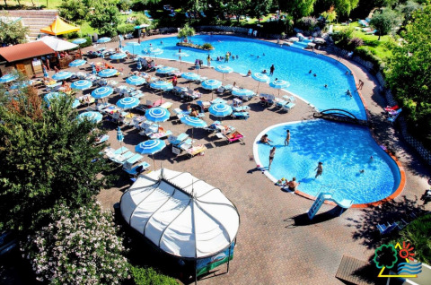 Buitenzwembad met ligstoelen en parasols bij DivaCamp San Marino, omgeven door groene bomen en natuur.