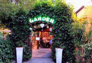 Ingang van DivaCamp San Marino - Safaritenten San Marino, omgeven door groen en een gezellige sfeer.