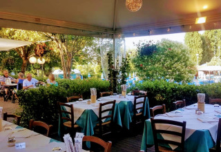 Buitenterras bij DivaCamp San Marino met gedekte tafels, omringd door groen en een ontspannen sfeer.