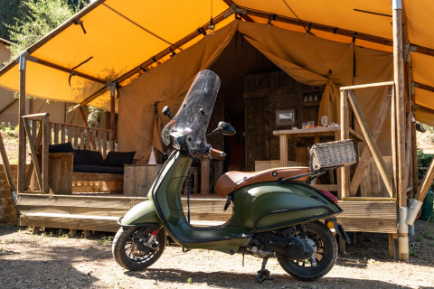 Een groene scooter staat geparkeerd voor een glampingtent bij DivaCamp San Marino - Safaritenten San Marino.