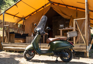 Een groene scooter staat geparkeerd voor een glampingtent bij DivaCamp San Marino - Safaritenten San Marino.