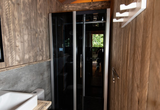 Moderne badkamer met houten wanden en glazen douche bij DivaCamp San Marino - Safaritenten San Marino.