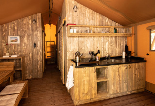 Binnenaanzicht van een DivaCamp San Marino safaritent met houten keuken en eethoek.