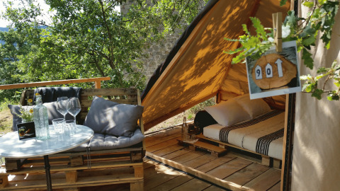 Glamping accommodation 'Novanta - Boomhut Toscane' with cozy outdoor seating and a comfy bed in a tent.