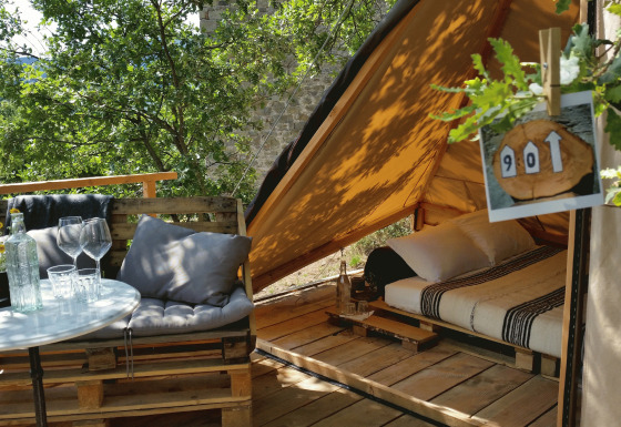 Glampingaccommodatie 'Novanta - Boomhut Toscane' met buitenzitje en comfortabel bed in een tent.