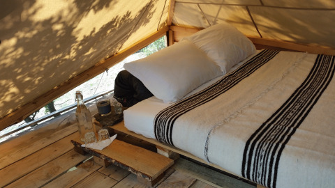 Innenaufnahme einer luxuriösen Glamping-Unterkunft mit gemütlichem Bett und Holzboden im Zelt.