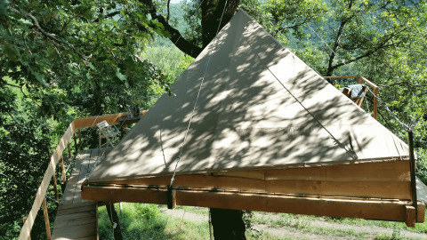 Hébergement glamping 'Novanta - Boomhut Toscane' avec tente et terrasse dans une cabane perchée en forêt.