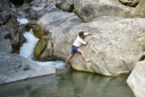 Hombre trepando descalzo por grandes rocas cerca de un arroyo junto al glamping Novanta - Boomhut Toscane en Toscana.