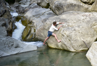 Un uomo scala a piedi nudi grandi rocce vicino a un ruscello, vicino al glamping Novanta - Boomhut Toscane in Toscana.