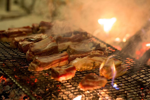 Jugosos trozos de carne asándose en una parrilla al fuego en Novanta - Boomhut Toscane, ideal para glamping.
