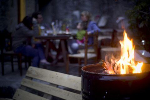 Glamping chez Novanta - Boomhut Toscane, feu de camp devant et invités détendus à table à l’arrière-plan.