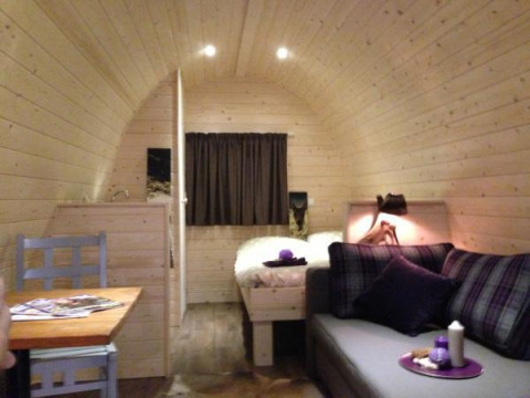 Interno di una cabina glamping accogliente con pareti in legno, divano, letto e tavolo da pranzo in Hessen.