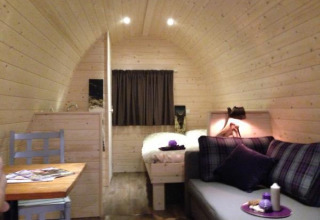 Cozy glamping cabin interior with wooden walls, a sofa, bed, small dining table and lamp in Hessen.