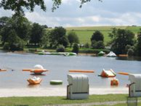 View of the lake at Campingpark am Gederner See with glamping, pedal boats and green hills in Hessen.