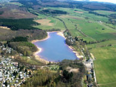 Luftaufnahme vom Campingpark am Gederner See, Glamping Hessen, mit See, Wiesen und Campingbereich.