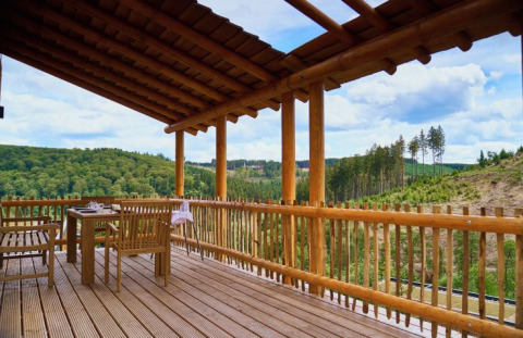 Wooden glamping terrace overlooking forested hills at UplandParcs Sauerland - Boomhutten, Germany.