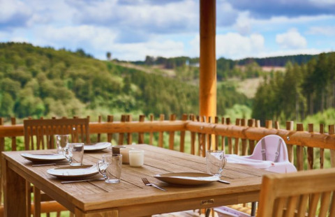 Essbereich auf einer Holzbalkonterrasse bei UplandParcs Sauerland - Boomhutten, mit Blick auf bewaldete Hügel.