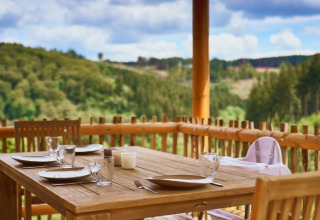Zona pranzo all'aperto su terrazza in legno a UplandParcs Sauerland - Boomhutten, vista sulle colline verdi.