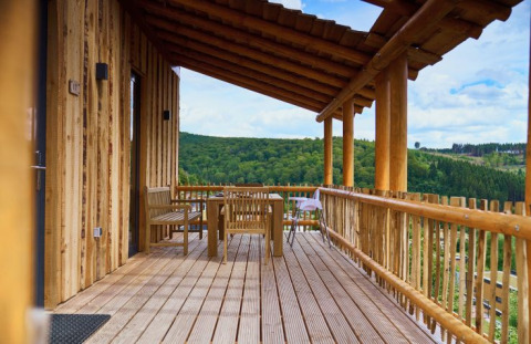 Træhytte med overdækket terrasse og udsigt over grønne bakker ved UplandParcs Sauerland, glamping i Tyskland.