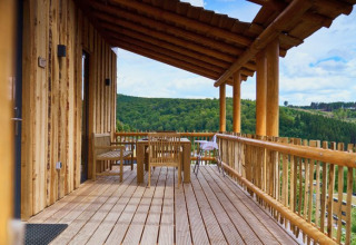 Træhytte med overdækket terrasse og udsigt over grønne bakker ved UplandParcs Sauerland, glamping i Tyskland.