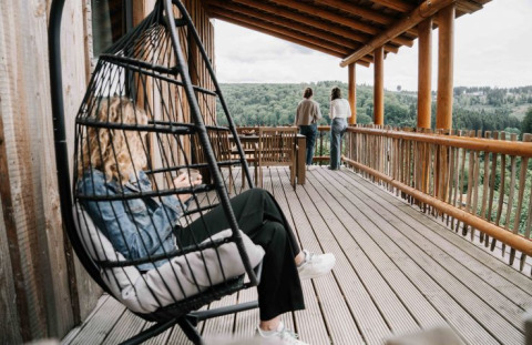 Person entspannt auf einer Hängeschaukel auf einer Holzterrasse, zwei genießen die Aussicht bei UplandParcs Sauerland.