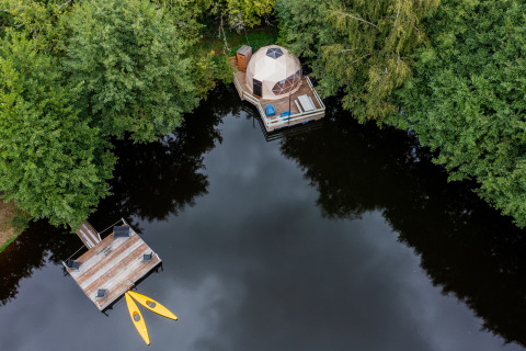 Vista aerea di Glamping Auvergne con cupola geodetica, pontile in legno e kayak su un lago circondato da alberi.