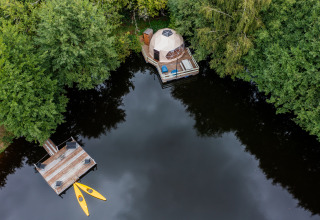 Vista aérea de Glamping Auvergne con domo geodésico, terraza de madera y kayaks junto a un lago rodeado de árboles.
