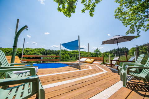 Zonnig terras met zwembad, ligstoelen en parasol bij Glamping Auvergne in Auvergne-Rhône-Alpes, Frankrijk.