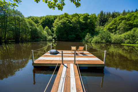 Pont flottant en bois avec transats sur un lac paisible, entouré de verdure au Glamping Auvergne.