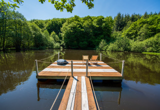 Pont flottant en bois avec transats sur un lac paisible, entouré de verdure au Glamping Auvergne.