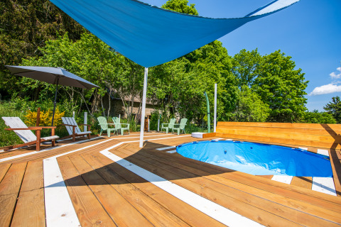 Glampingplatz in Auvergne-Rhône-Alpes mit Pool, Holzdeck, Sitzgelegenheiten und Sonnensegel im Freien.