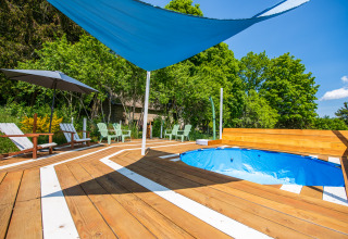Espace glamping extérieur en Auvergne-Rhône-Alpes avec piscine, terrasse en bois, chaises et voile d'ombrage.