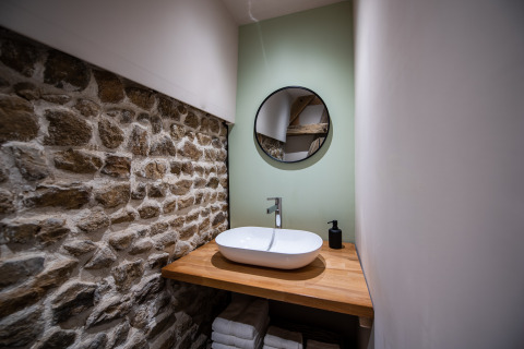Modern glamping bathroom with stone wall, wooden countertop, round sink and mirror in Auvergne-Rhone-Alpes.