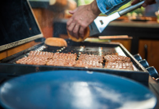 Une personne fait griller des burgers et des pains au Glamping Auvergne – Glampingtenten Auvergne-Rhone-Alpes.